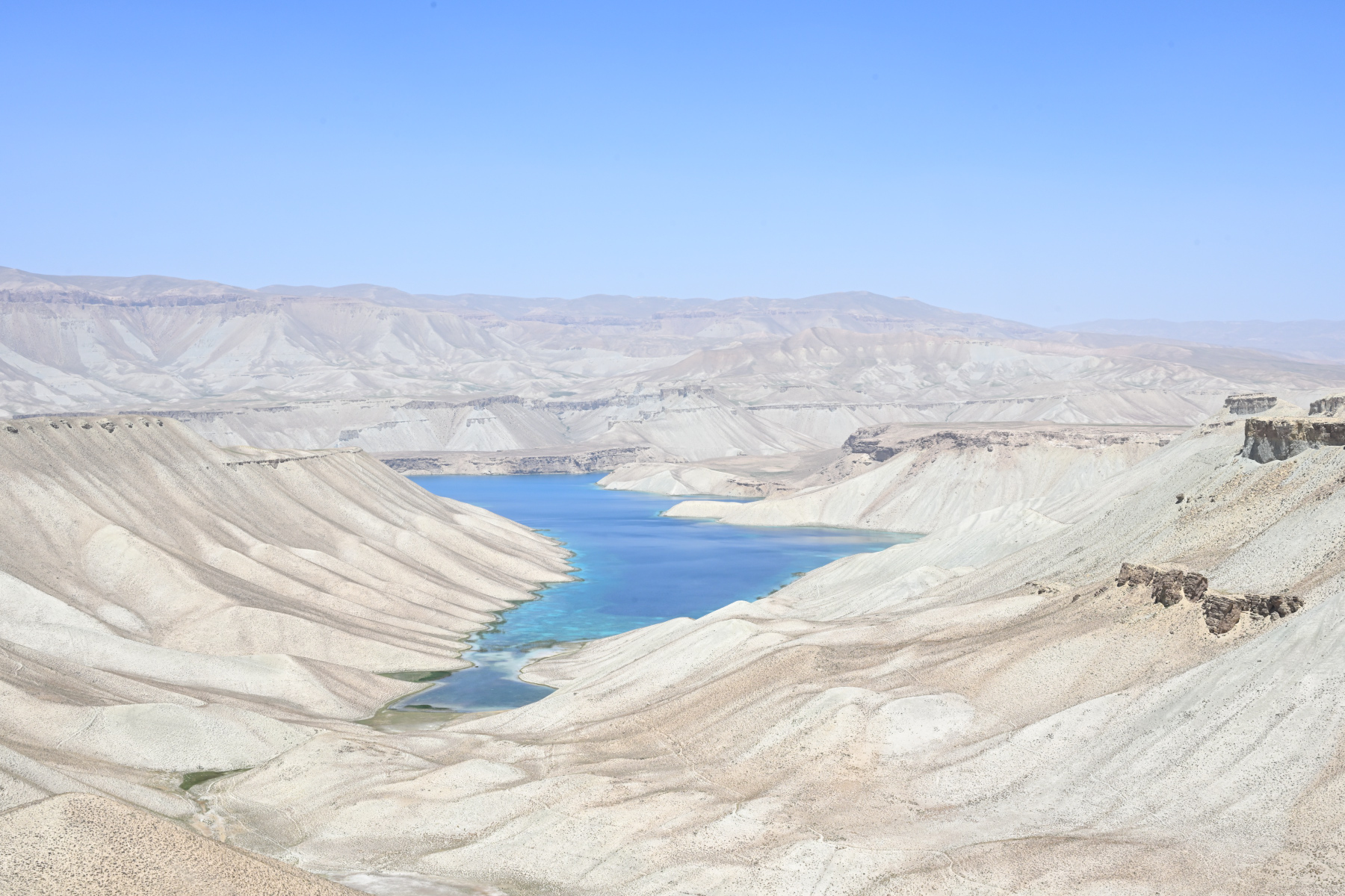 A turquoise lake at Band-e-Amir framed by pale travertine cliffs, ridgelines receding into haze.